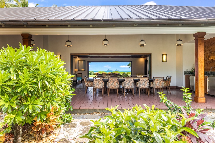 Covered dining lanai framed by tropical landscaping and panoramic ocean views.