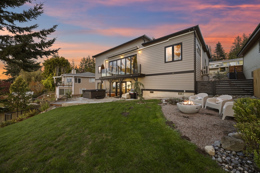 Twilight view of the home and lawn — glowing windows, cozy firepit, and a serene close to a day by the bay.