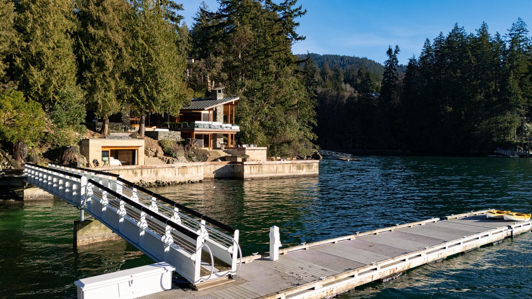Modern lakefront property nestled among tall evergreens with private dock and scenic forested hills.