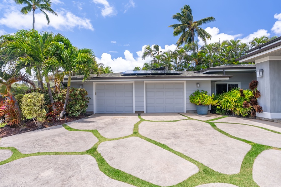Tropical greenery frames the clean, spacious driveway and garage.