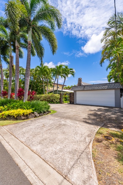 Palm-lined driveway leads to a spacious private garage, with vibrant tropical landscaping and colorful gardens framing the entrance to this island-style retreat.