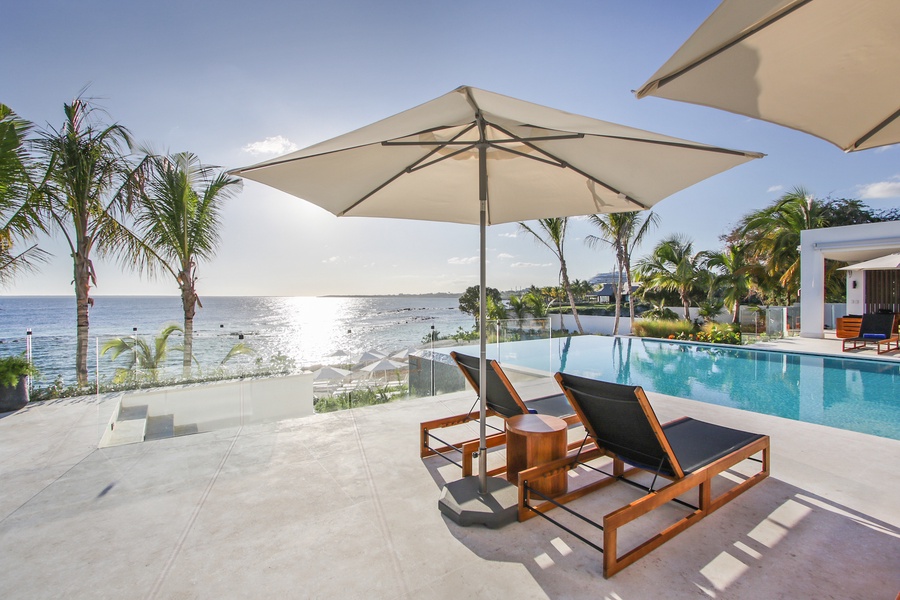 Poolside sun loungers with umbrellas, overlooking the ocean.