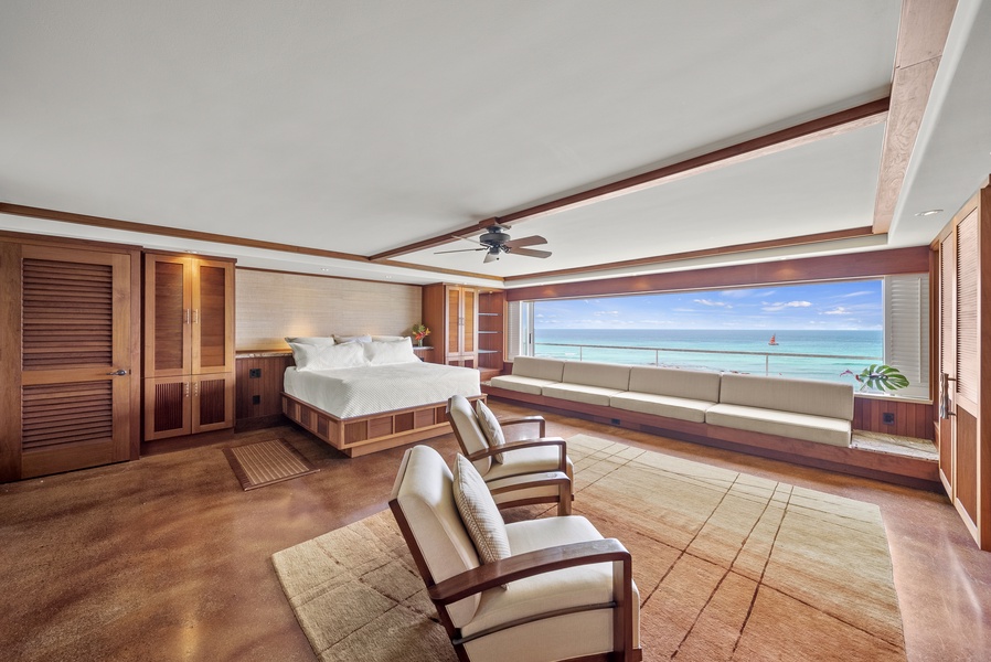 The sleeping space includes a bed, ocean-facing sofa-style seating, and two additional chairs