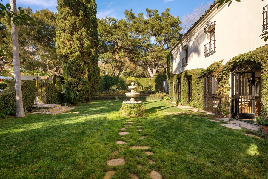 Elegant Mediterranean villa with beautifully manicured gardens and charming ivy-covered facade in a peaceful setting.