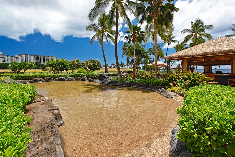 The sand-bottom pool offers a fun and safe play area for children, surrounded by a Hawaiian resort atmosphere.