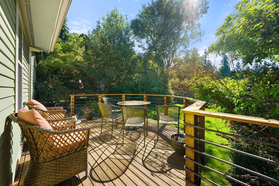 Step onto your private deck with cozy wicker seating and soak up peaceful garden views through the sunny afternoon light.