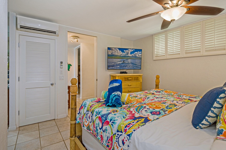 This cozy bedroom features a colorful, tropical design with modern amenities, including a wall-mounted TV for entertainment and air conditioning for comfort