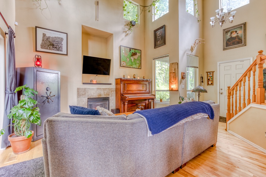 The comfortable living room furnished with an oversized couch, a flat-screen TV, a gas fireplace, an entire bookshelf, a piano, a large safe, and plenty of fresh plants is a great space to unwind