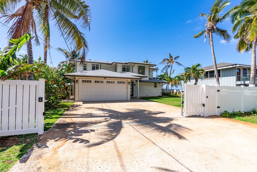 A wide driveway framed by palms leads to the spacious two-car garage and main estate entrance.