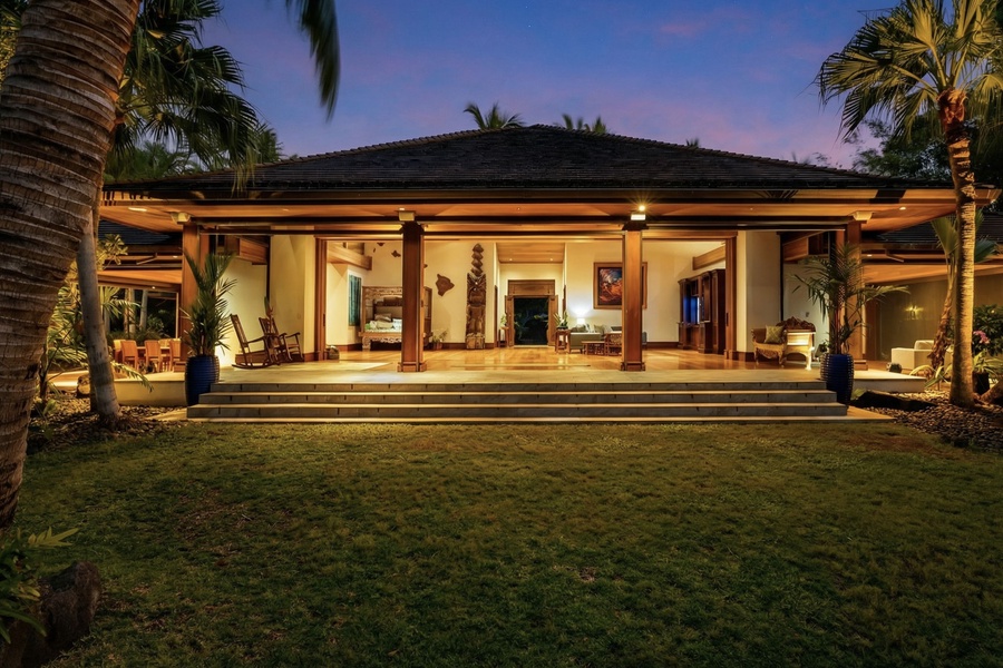 Tropical villa exterior showcasing open-air design with warm lighting and lush palm trees in the evening twilight.
