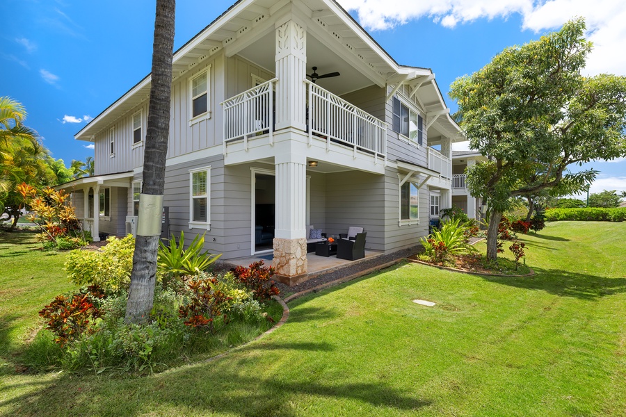 Elegant two-story vacation home with tropical landscaping and covered lanai seating area surrounded by lush gardens and palm trees.