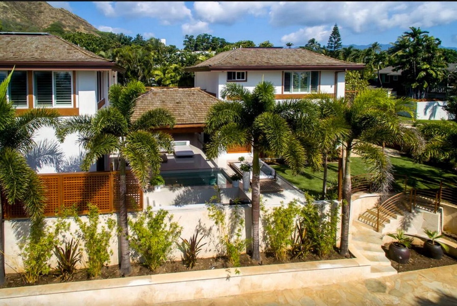 Palms and trimmed hedges screen the guest house entrance from the road.