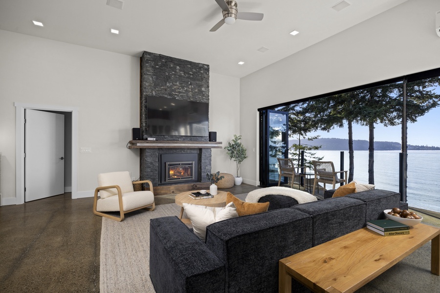 Inviting living room with cozy fireplace and full wall of glass showcasing sweeping views of Bellingham Bay.