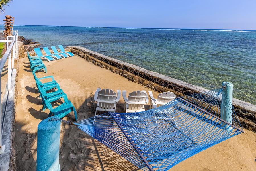 A hammock and chairs at the water's edge, reef stretching out just beyond the wall.