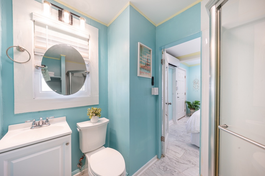 Bright bathroom with turquoise walls, a round mirror, and clean, modern finishes.