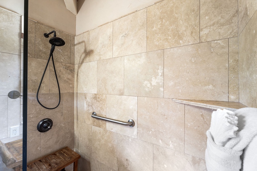 Stone tile walk-in shower with grab bar—elegant and accessible with timeless finishes.