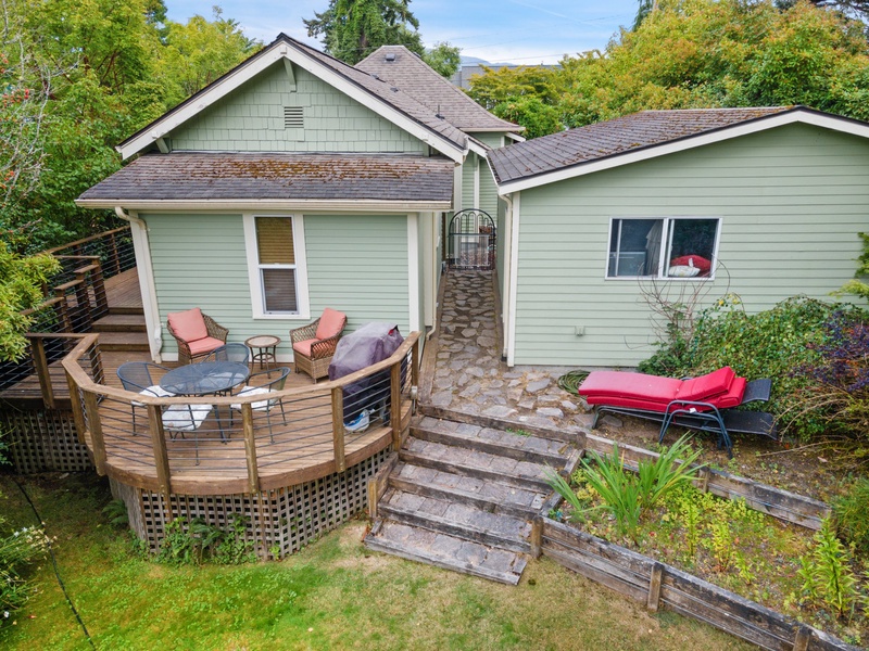 Charming green cottage nestled among mature trees with a welcoming curved deck and stone walkway connecting the main house to guest quarters.