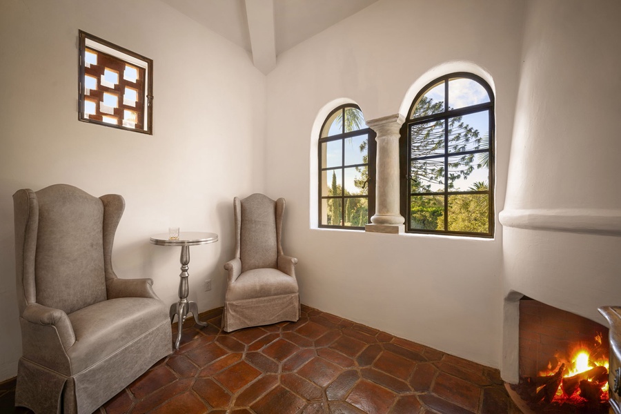 Settle into soft wingback chairs beside a flickering fireplace, framed by arched windows that offer tranquil views of the garden beyond.