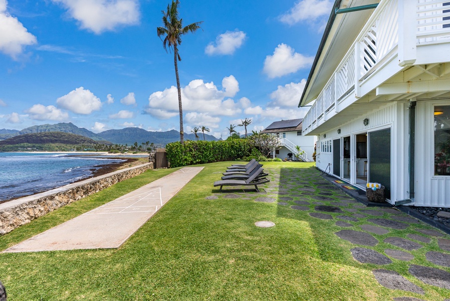 A beachfront property featuring pristine lawn area with lounge chairs overlooking tropical coastline and dramatic mountain backdrop.