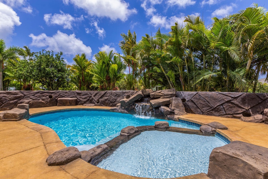 Lani Oasis pool with waterfall feature, shallow entry, and lush tropical backdrop.