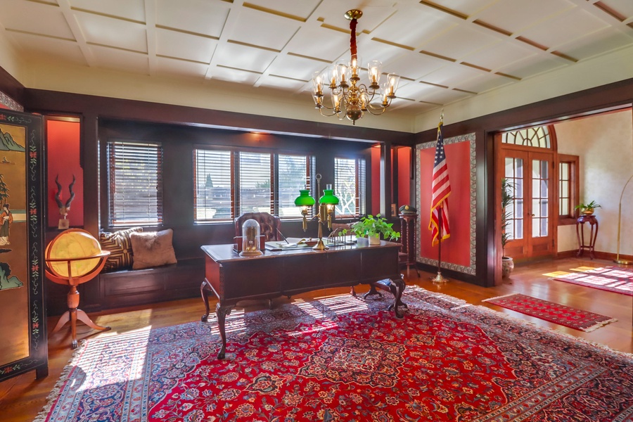 This office space has rich wood accents, a classic chandelier, and ample natural light, perfect for focused work or leisurely reading.