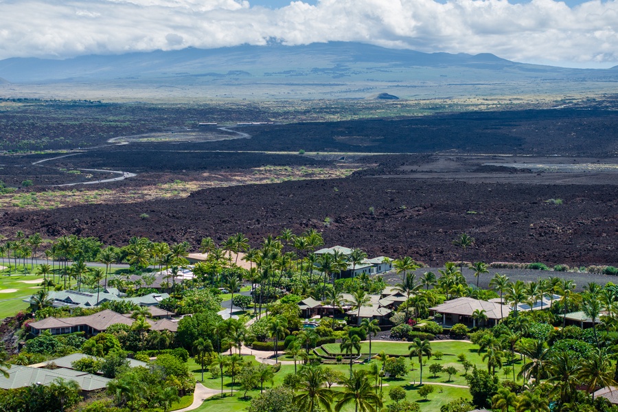 An aerial view showcasing tropical homes with a backdrop of lush mountains and volcanic terrain.