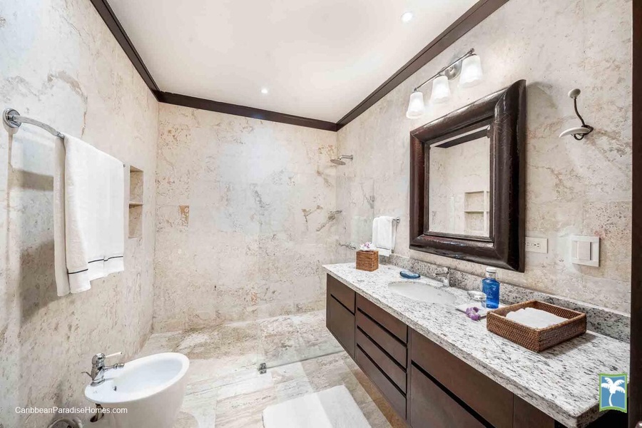 Modern ensuite bathroom featuring a granite countertop, large mirror, and a glass-enclosed shower.