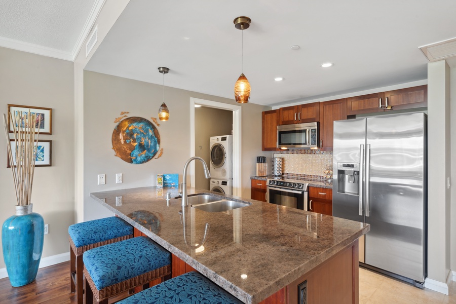 The modern kitchen at Honua Kai Konea 204 includes granite countertops, custom lighting, and bar seating.