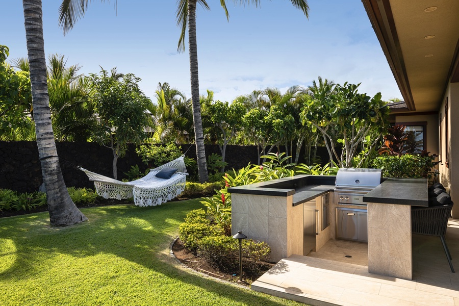 BBQ grill area with ample prep space and mini fridge, with grassy private yard and hammock beyond.