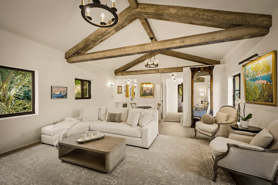 The cottage's living room has exposed wooden beams, plush seating, and natural light streaming through picture windows.