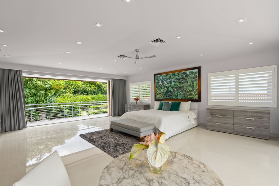 Step into your serene bedroom retreat, where a plush king bed awaits beneath artwork that celebrates tropical beauty. Slide open the glass doors to your private balcony overlooking lush greenery, and unwind in modern comfort.