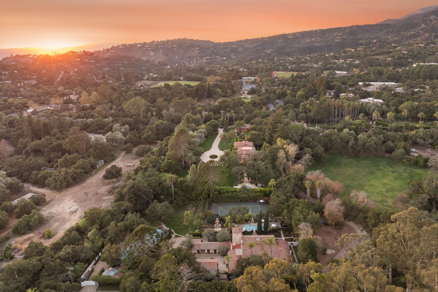 Sprawling estate nestled in rolling hills with tennis court and pool, captured during golden sunset over the scenic valley.