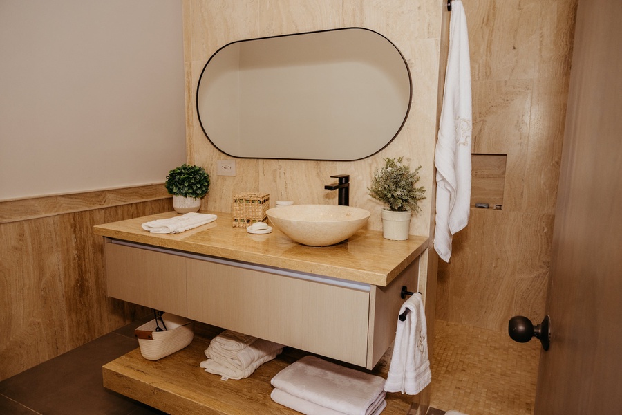 Contemporary ensuite bathroom with a sleek countertop, oval mirror, and chic vessel sink.
