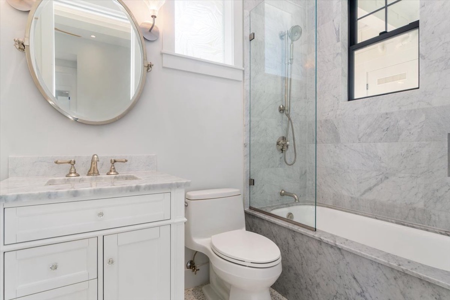 Elegant guest bath with marble tub surround, sleek vanity, and modern fixtures.