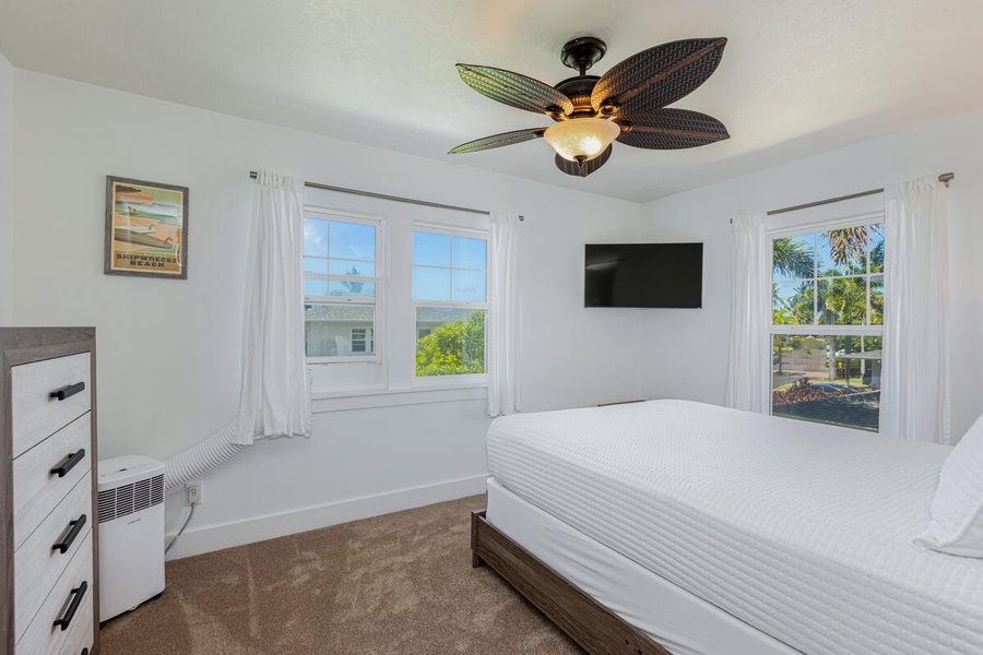 Guest bedroom with ceiling fan, queen bed, and peaceful green views through large windows.