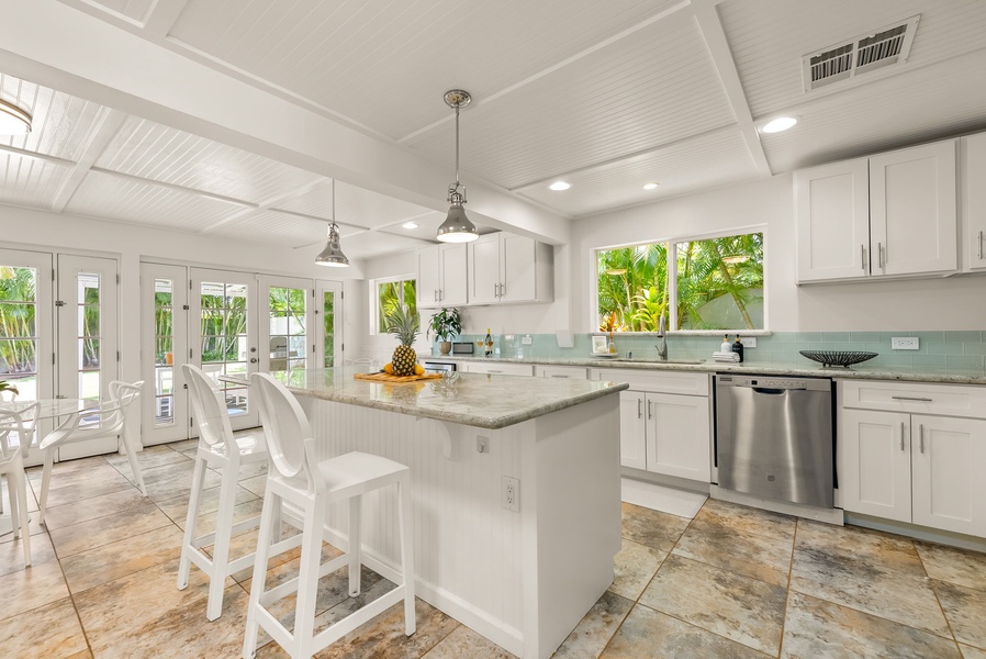 Step into your bright, coastal-inspired kitchen with white cabinetry, granite counters, and stainless appliances. Large windows frame lush palm views, flooding the space with natural light.