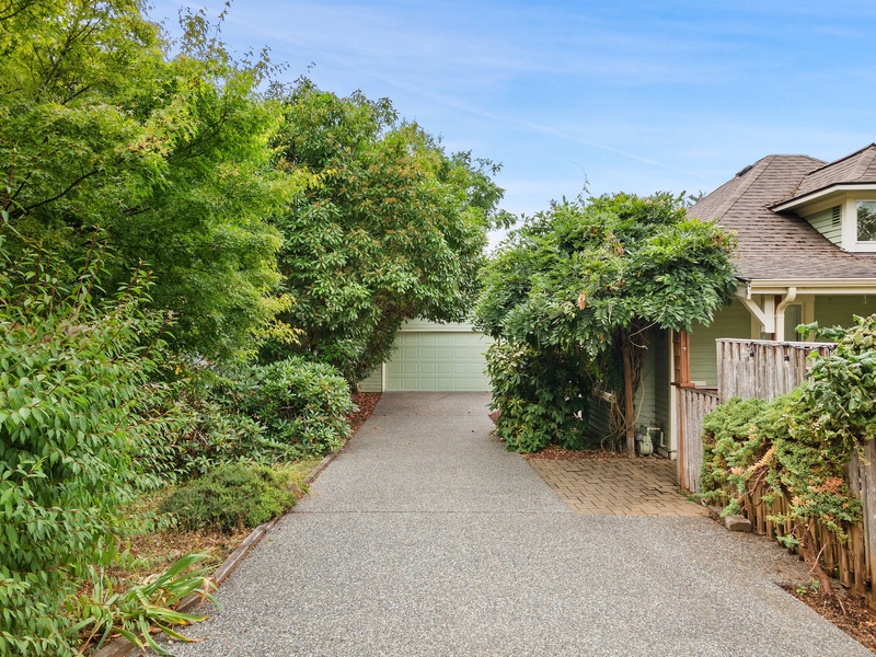 Peaceful driveway leads to private garage, surrounded by lush greenery and mature trees in a quiet residential setting.