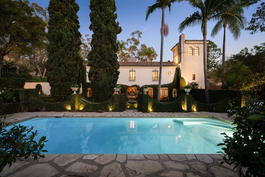 Mediterranean elegance meets tropical paradise with this stunning villa featuring illuminated palm trees and pristine pool surrounded by lush landscaping.