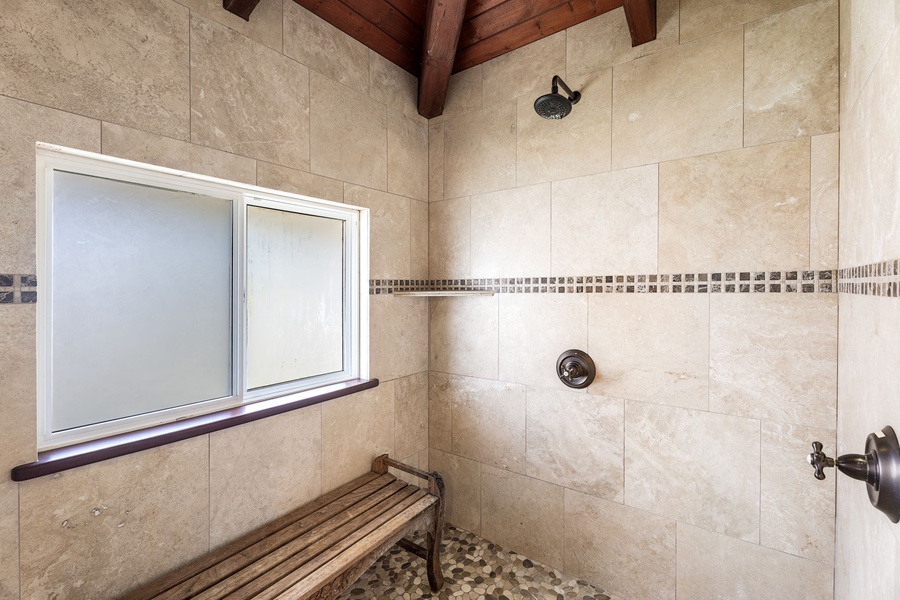 Private steam shower with stone floors and bench—tucked beneath a vaulted ceiling for an outdoor feel.