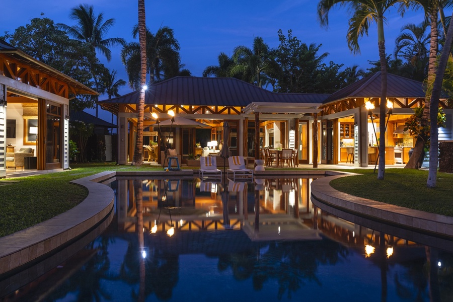 A tranquil view of the dining room, living room, and kitchen, illuminated by tiki torches across the serene pool