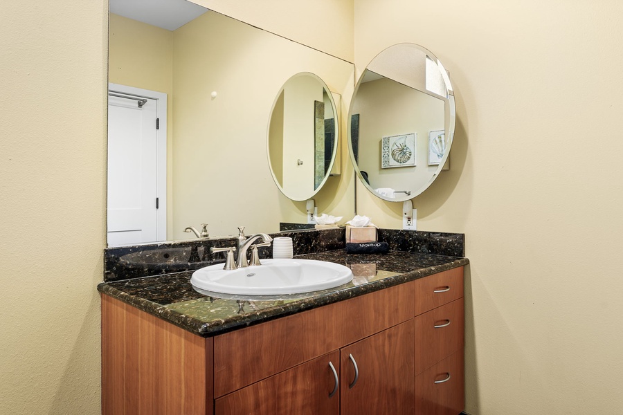 Elegant bathroom with a circular mirror, rich wood cabinetry, and granite countertop.