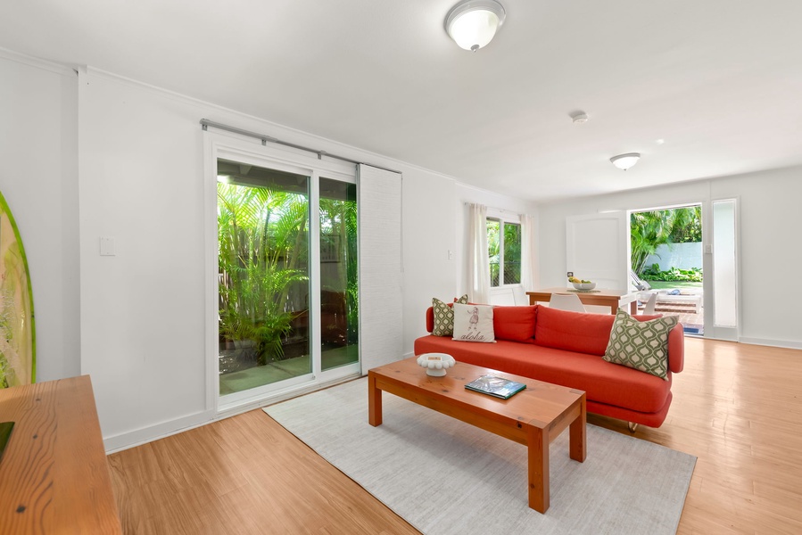 Relax on the vibrant coral sofa in your spacious living area, where sliding glass doors open to lush tropical greenery and seamlessly connect indoor and outdoor living.