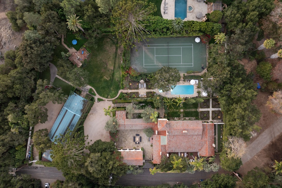 Expansive estate showcasing tennis court, multiple pools, and lush gardens surrounded by mature tropical landscaping.