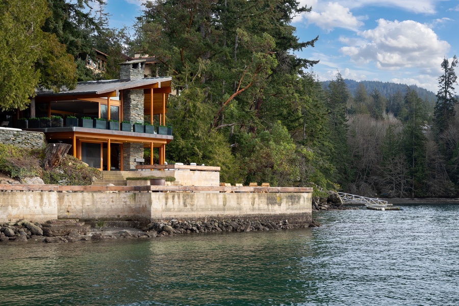 Modern waterfront property featuring contemporary architecture with natural stone and wood elements nestled among towering evergreens.