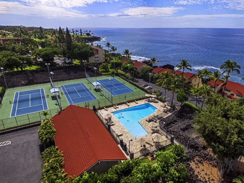Aerial view of the pool and of the tennis court nestled in lush greenery.