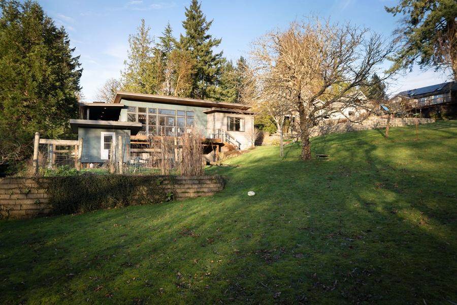 Modern property nestled among mature trees with expansive lawn area and neighboring homes visible in the peaceful residential setting.