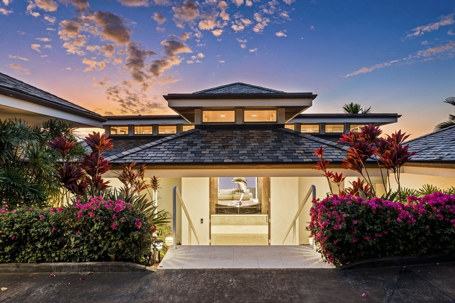 Modern tropical villa facade illuminated at sunset, featuring vibrant landscaping and elegant architectural design.