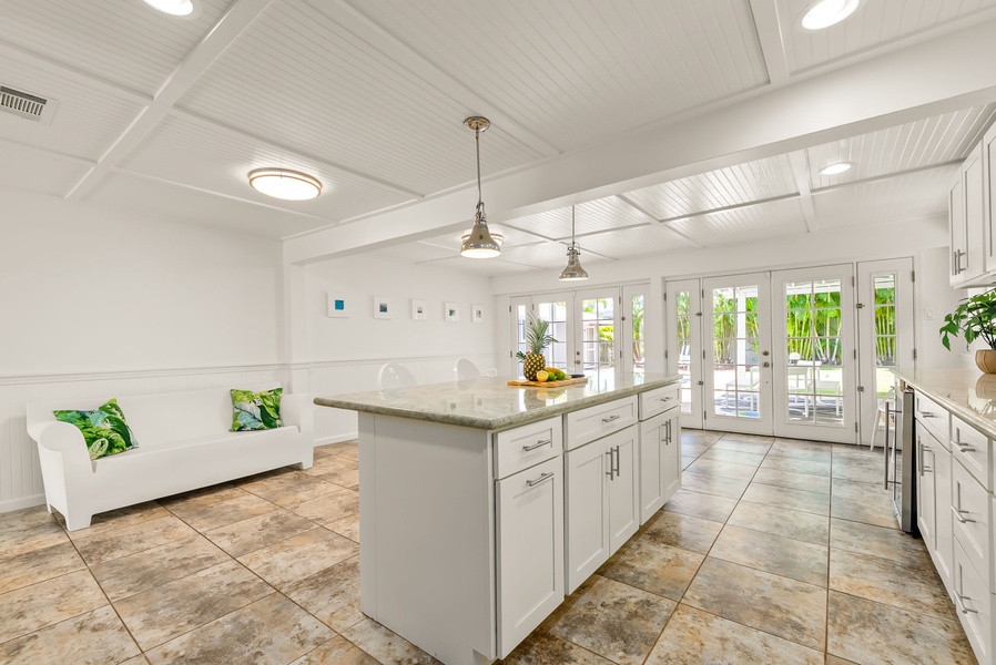Your bright, airy kitchen and lounge await—marble counters, tropical touches, and sunlight streaming through French doors to the patio.
