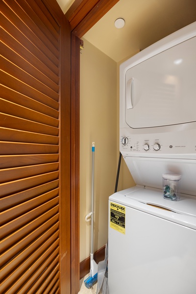Compact laundry space with stacked appliances and cleaning tools, neatly tucked away.