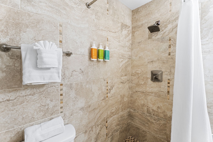 Unwind in your luxurious stone-tiled shower with rainfall showerhead, premium amenities, and plush towels awaiting your arrival.